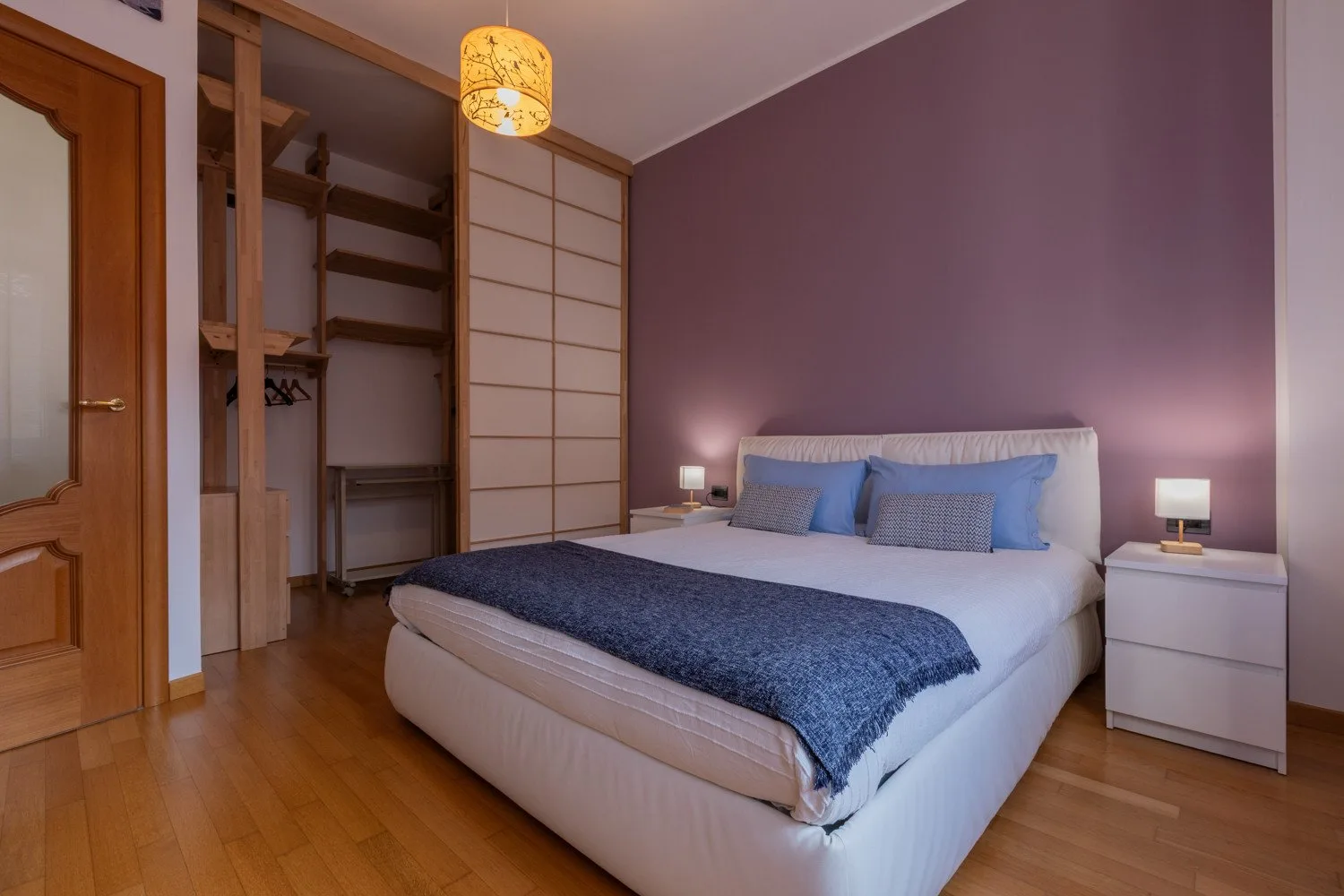 Un dormitorio con una cama, mesitas de noche y un armario abierto.