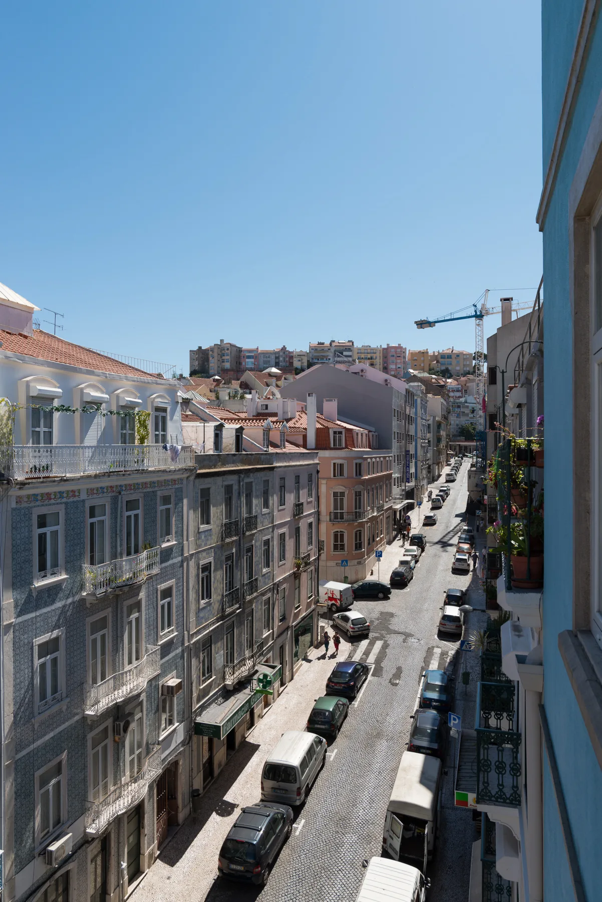 Una calle urbana estrecha flanqueada por edificios y coches aparcados bajo un cielo despejado.