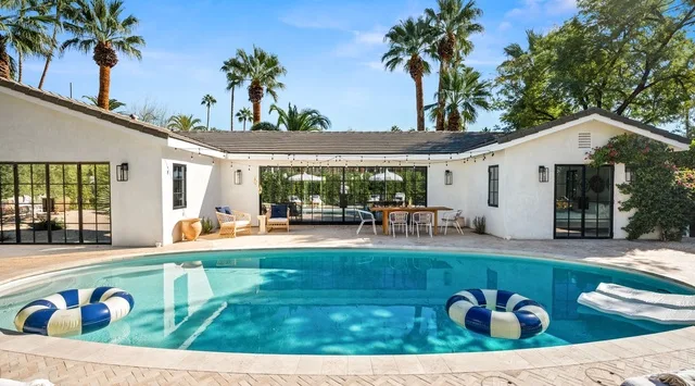 Una piscina en el patio está junto a una casa blanca, con asientos al aire libre y palmeras.