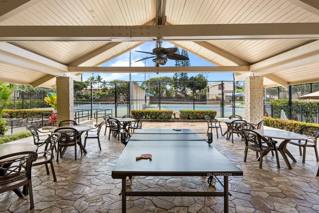 Una zona recreativa exterior cubierta tiene una mesa de ping-pong y asientos.