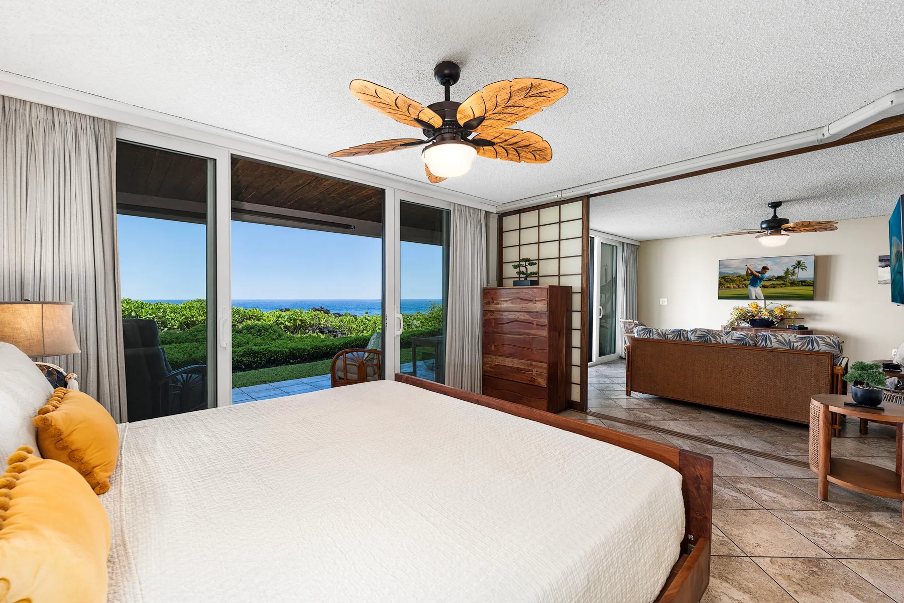 Un dormitorio con una cama grande junto a ventanas con vistas a la vegetación y al océano.