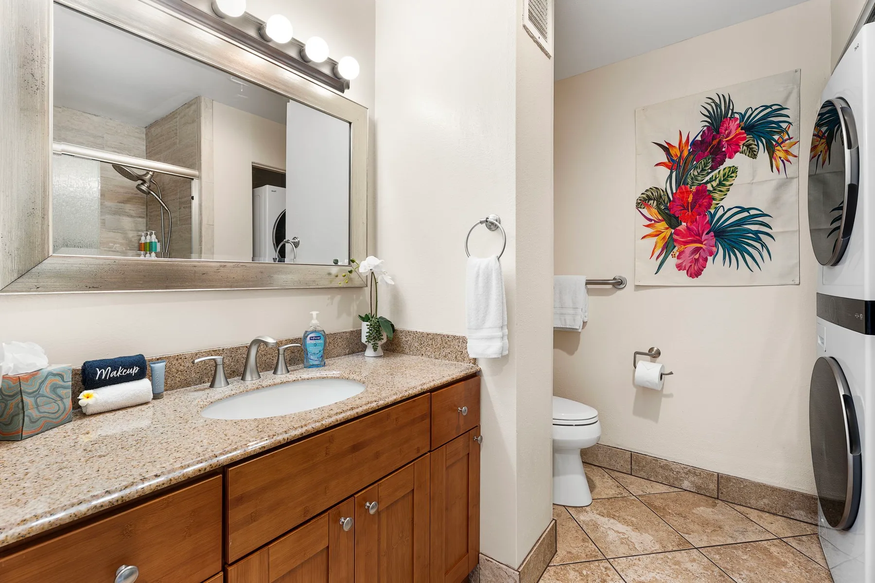 Un tocador de baño con lavabo y espejo junto a un inodoro y máquinas de lavandería.