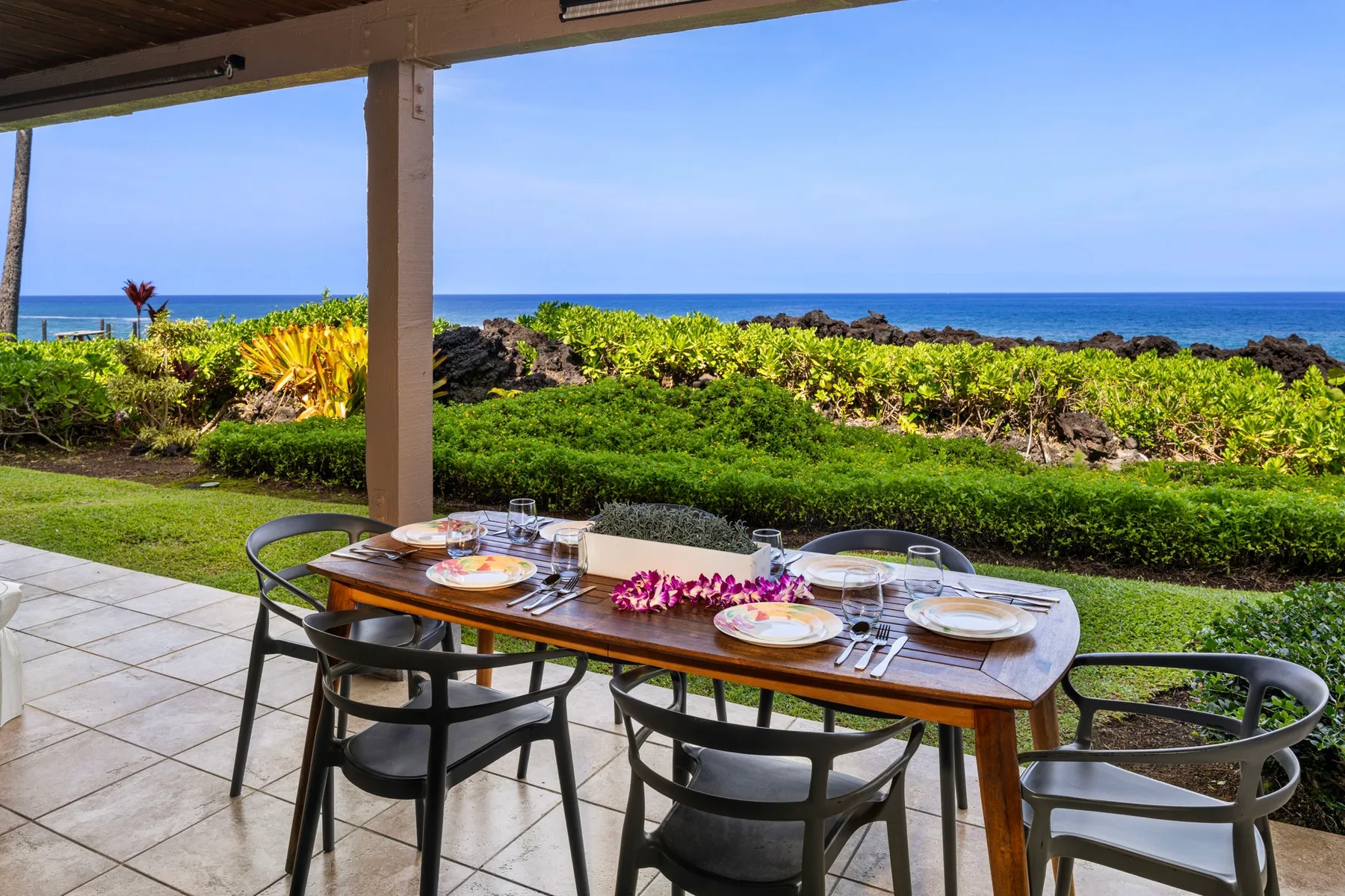 Una zona de comedor al aire libre cubierta mira al océano, con una mesa preparada para comer.