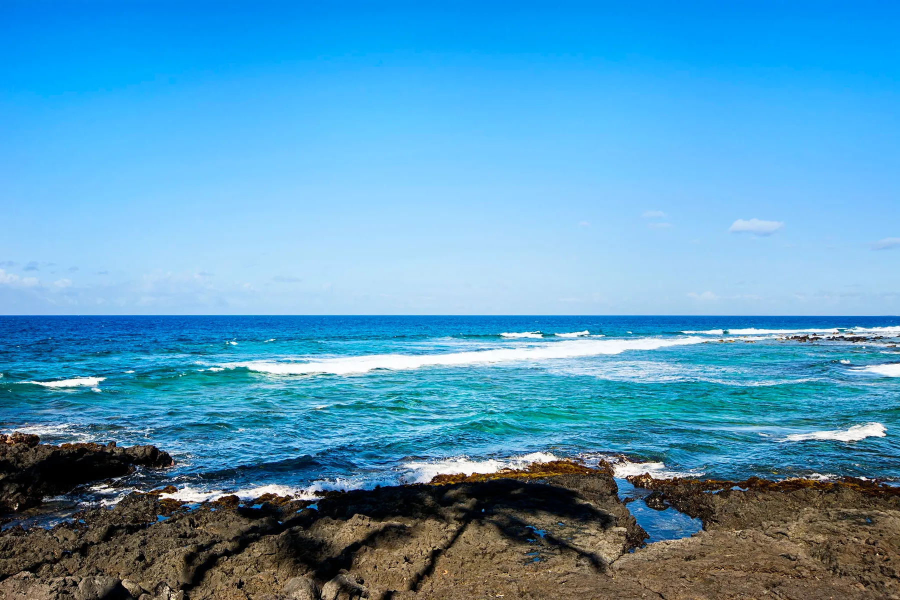 Las olas rompen junto a una costa rocosa bajo un cielo azul despejado.
