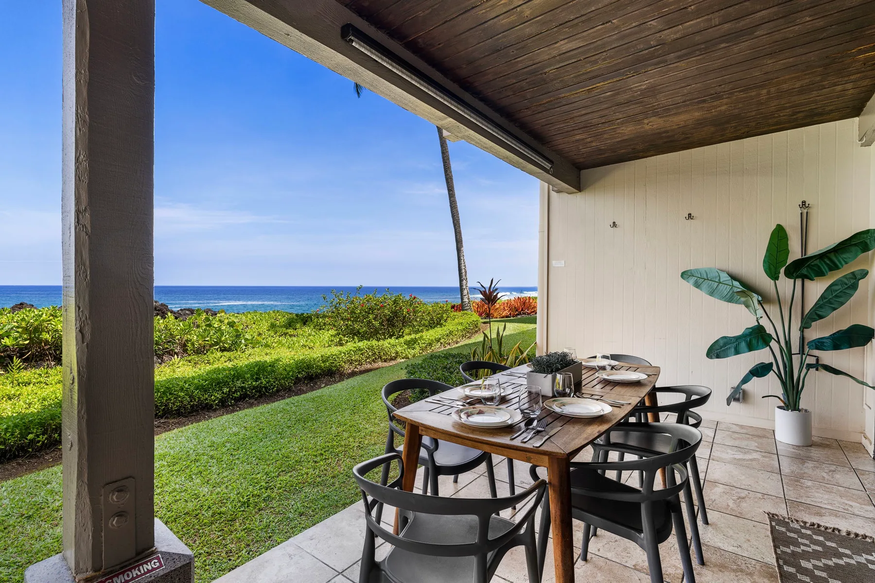 Una zona de comedor exterior cubierta da a un césped verde y al océano.