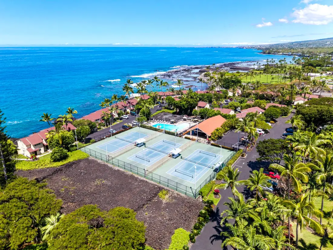 Vista aérea de un complejo junto al mar con canchas de tenis y palmeras.