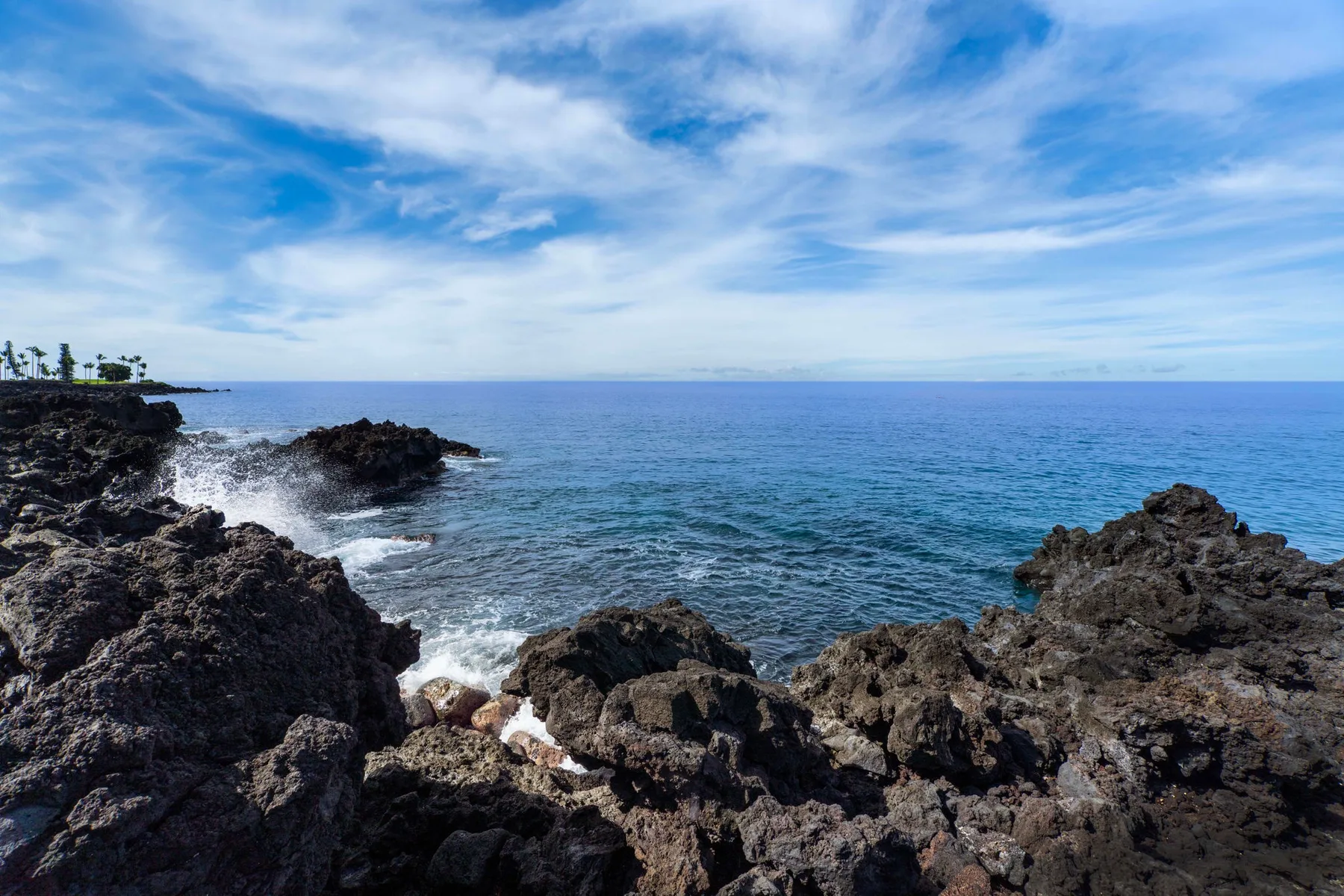 Costa rocosa junto al océano azul bajo un cielo nublado.