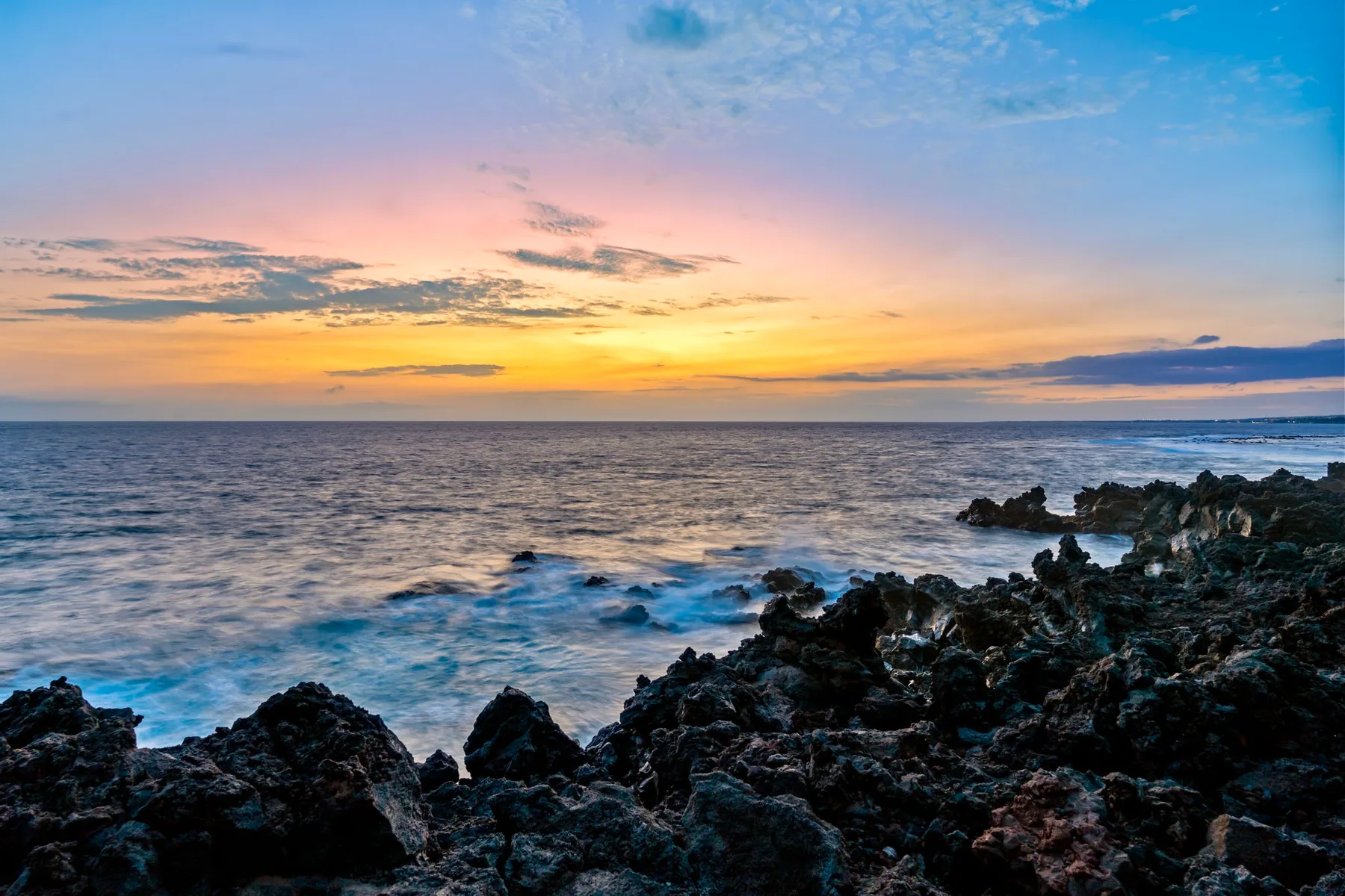 Costa rocosa y olas del océano bajo un cielo colorido al atardecer.