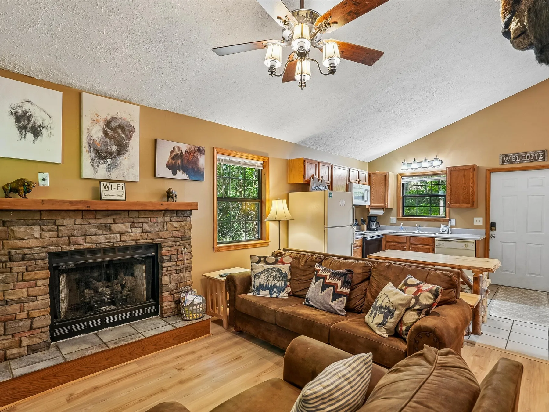 A living room opens into a kitchen, with a stone fireplace and seating.