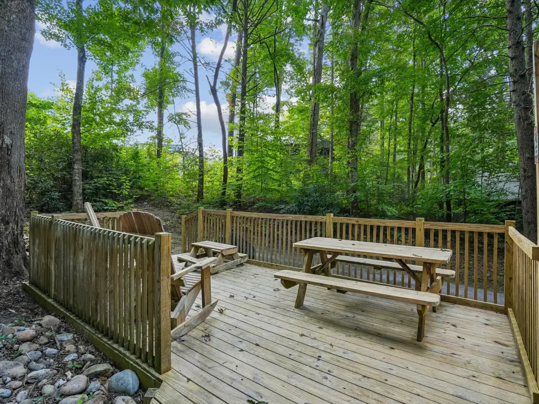 A wooden deck with picnic tables sits among leafy trees.