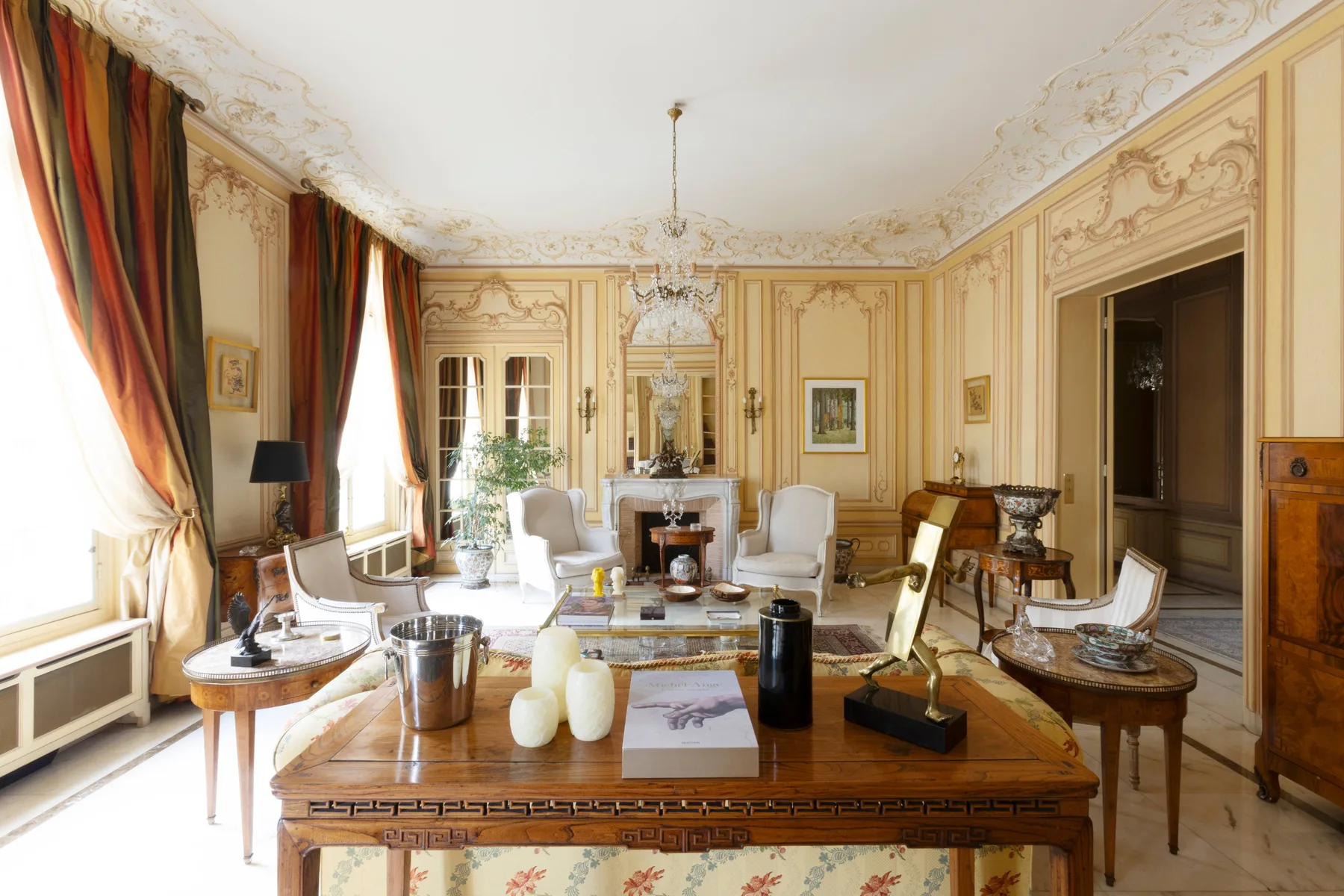An ornate sitting room with a fireplace and a large table in the foreground.