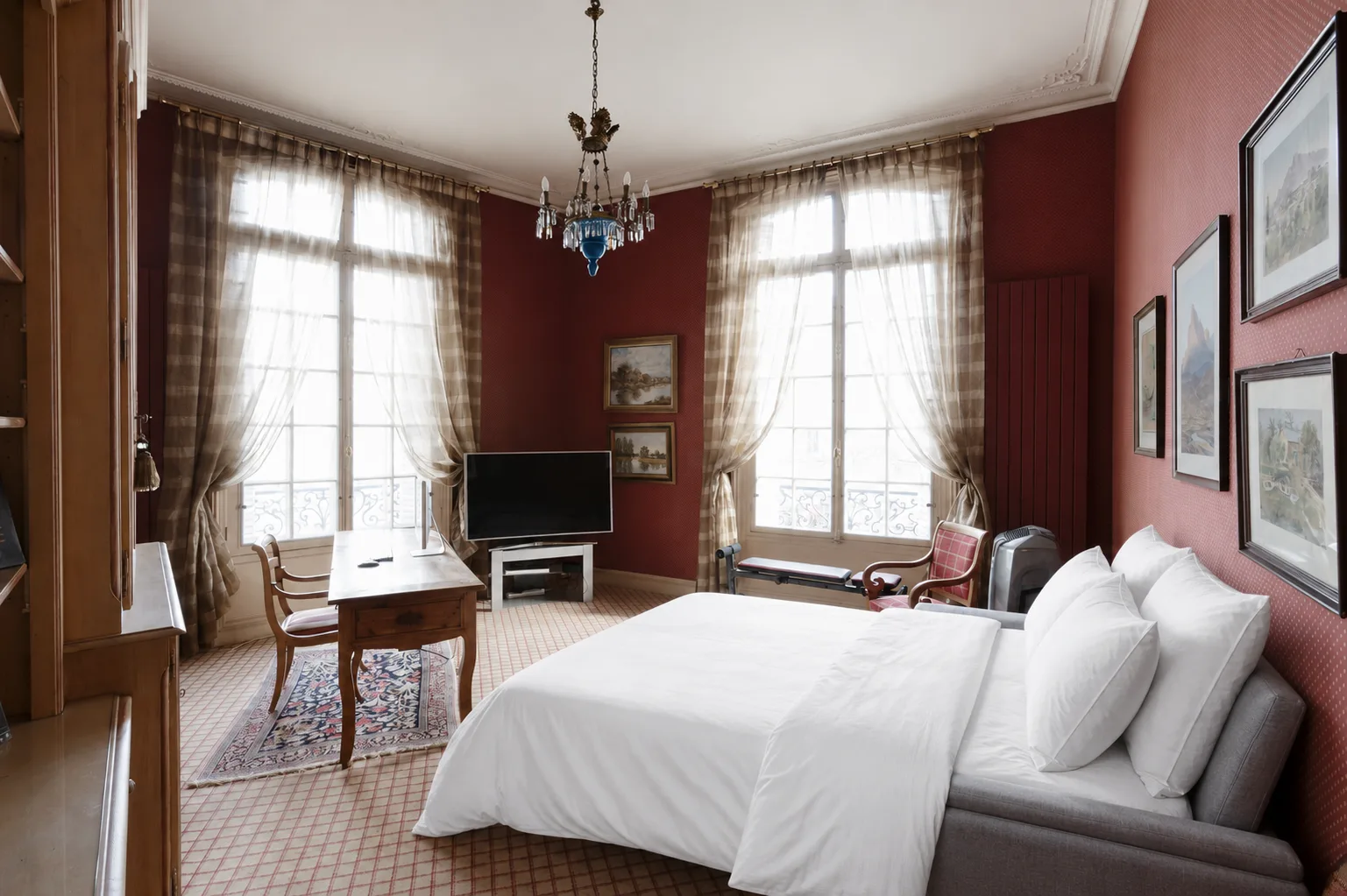 A bedroom with a large bed, tall windows, and a television.
