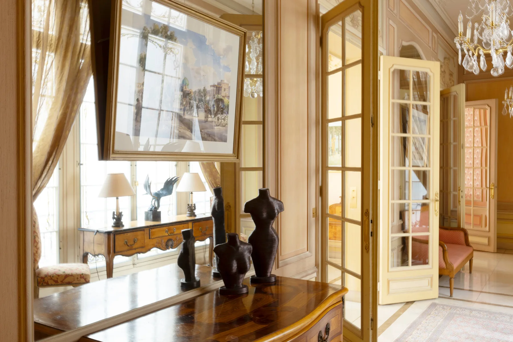 Una sala de estar ornamentada con ventanas altas, cuadros y muebles de madera oscura.