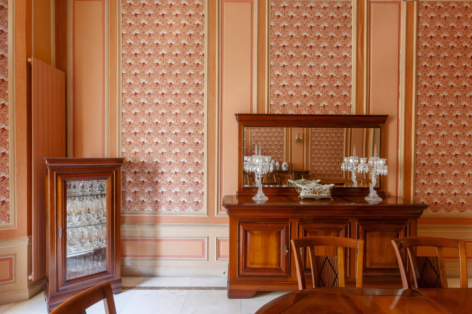 Un comedor con un aparador de madera, un espejo y papel tapiz estampado.