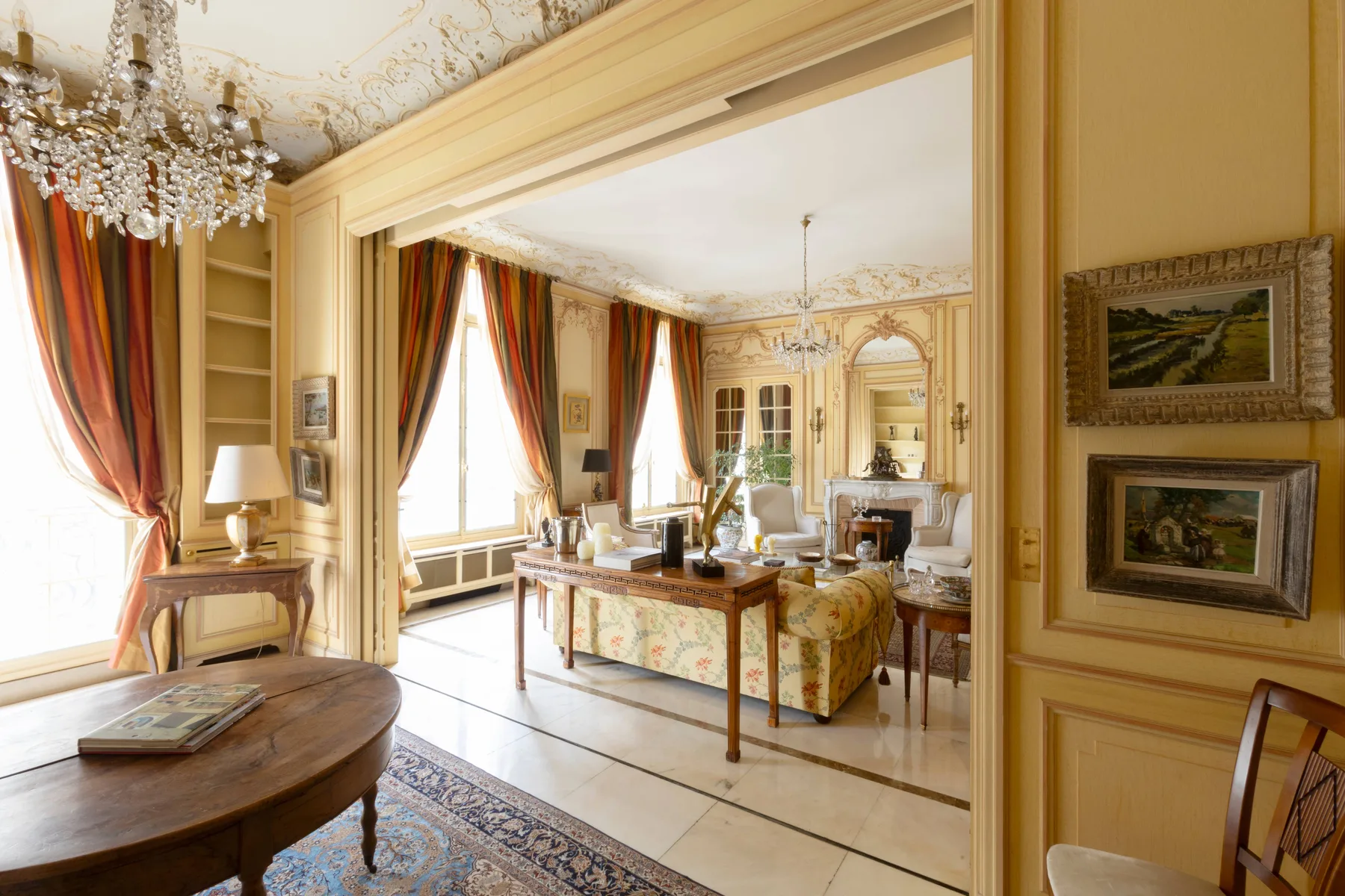Una sala de estar ornamentada, con ventanas altas, cortinas y una zona de asientos central.