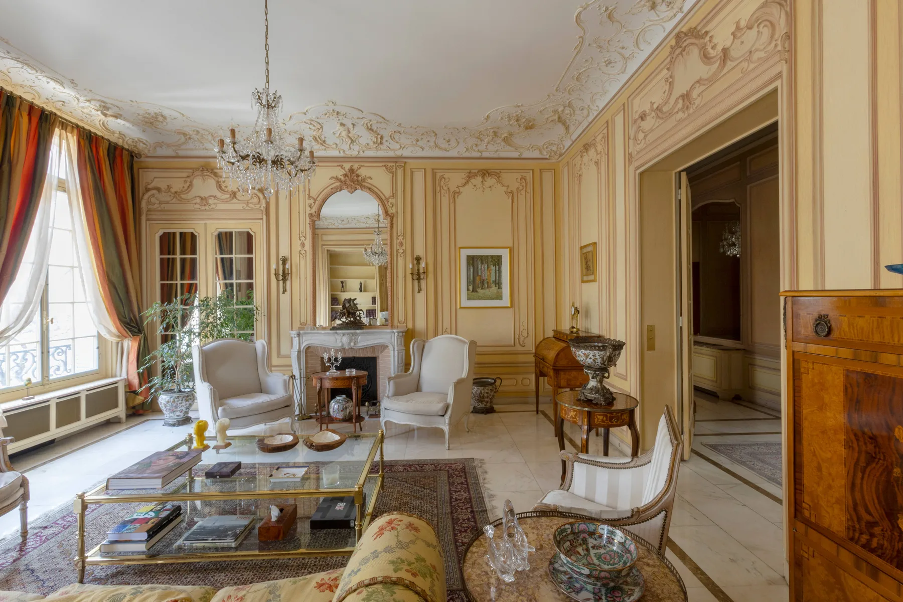 Un salón ornamentado con paneles decorativos, una lámpara de araña y asientos alrededor de una chimenea.
