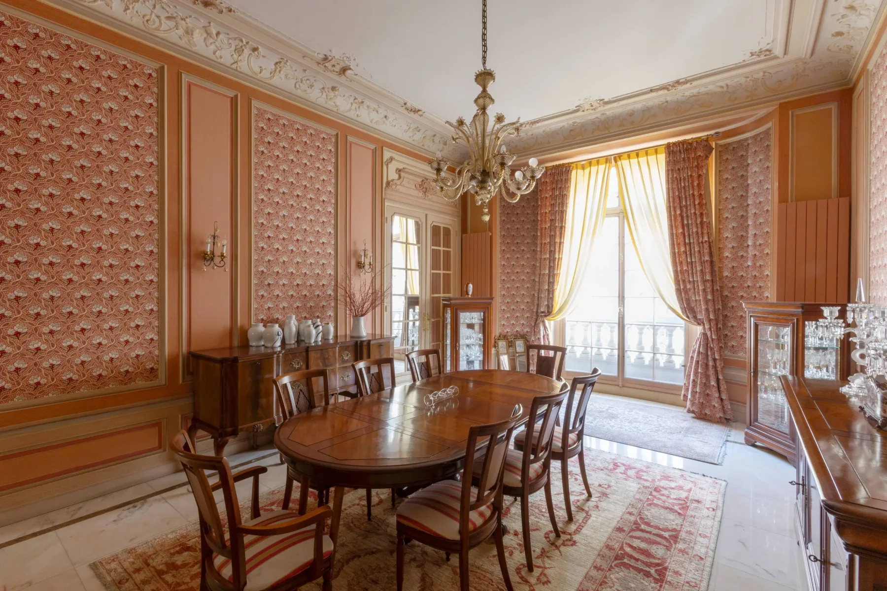 Un comedor ornamentado con una larga mesa de madera y altas ventanas con cortinas.