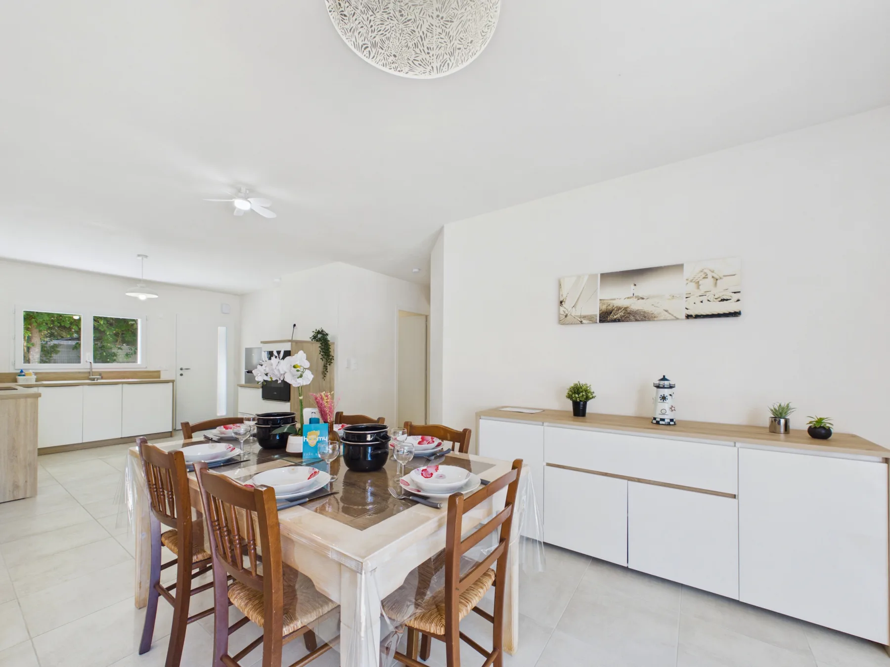 A bright dining area with a wooden table and chairs beside a white kitchen.