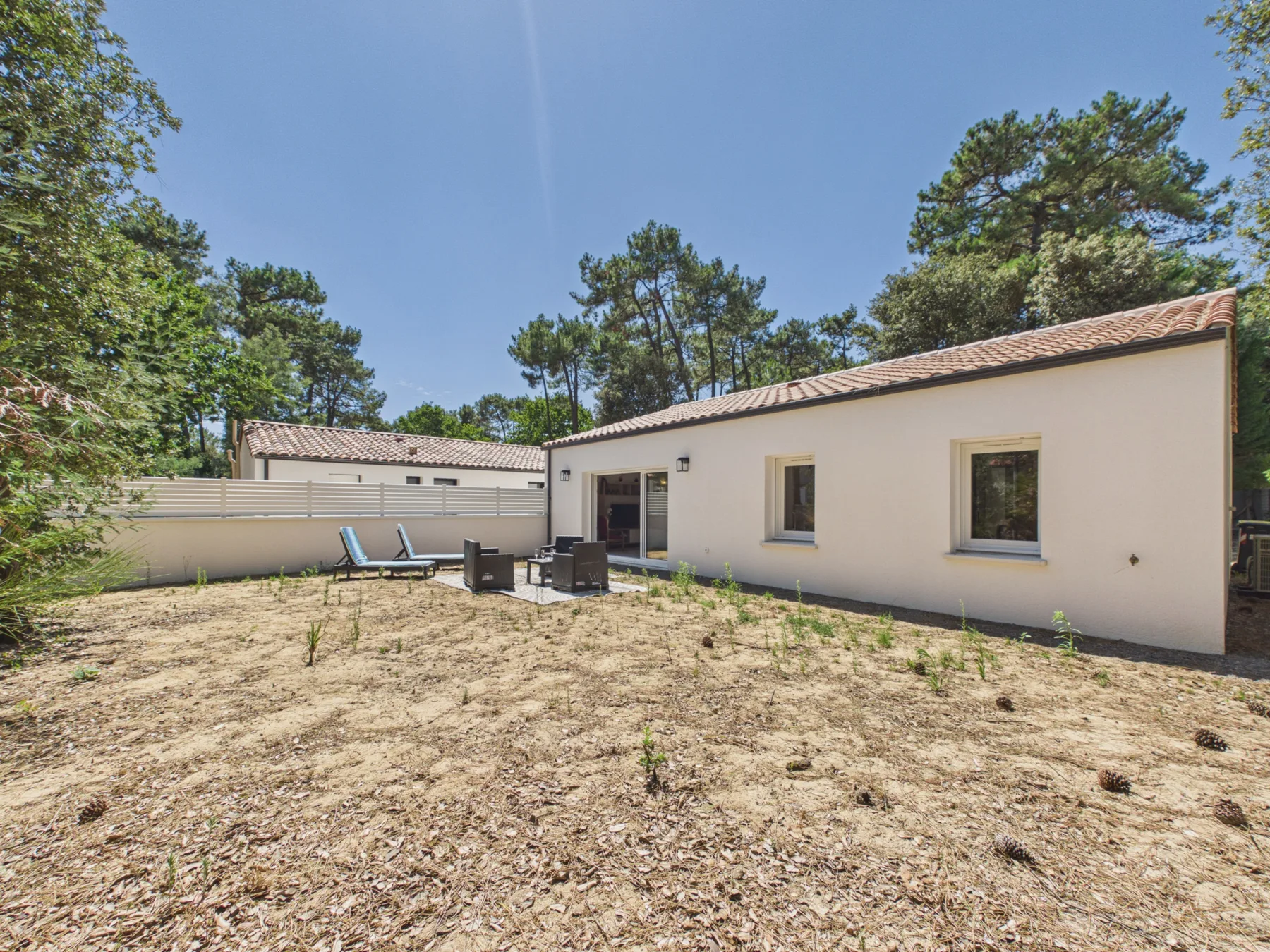 A single-story house with a patio and outdoor seating beside a dry garden.