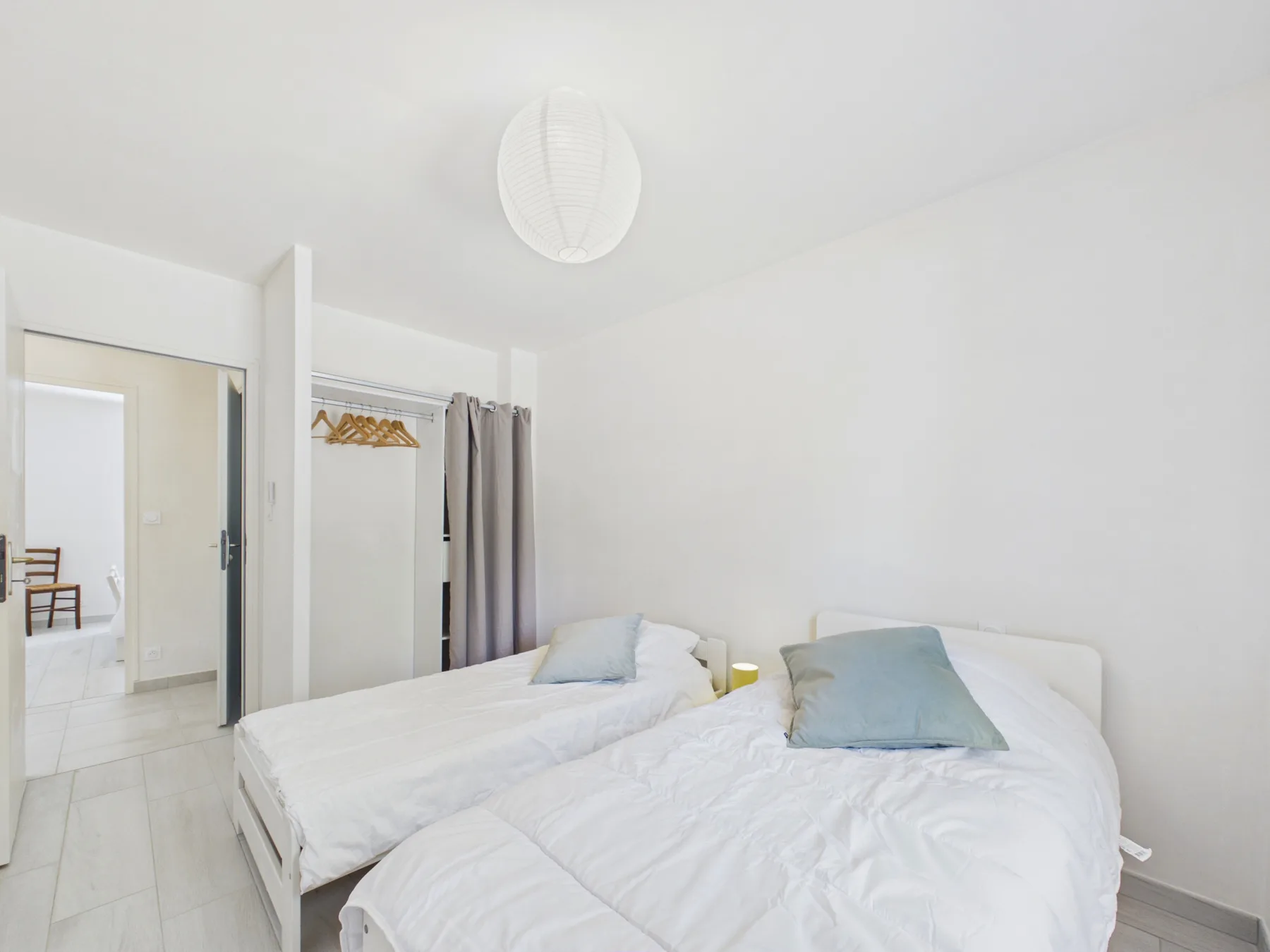 A bright bedroom with two beds, white bedding, and a wardrobe.