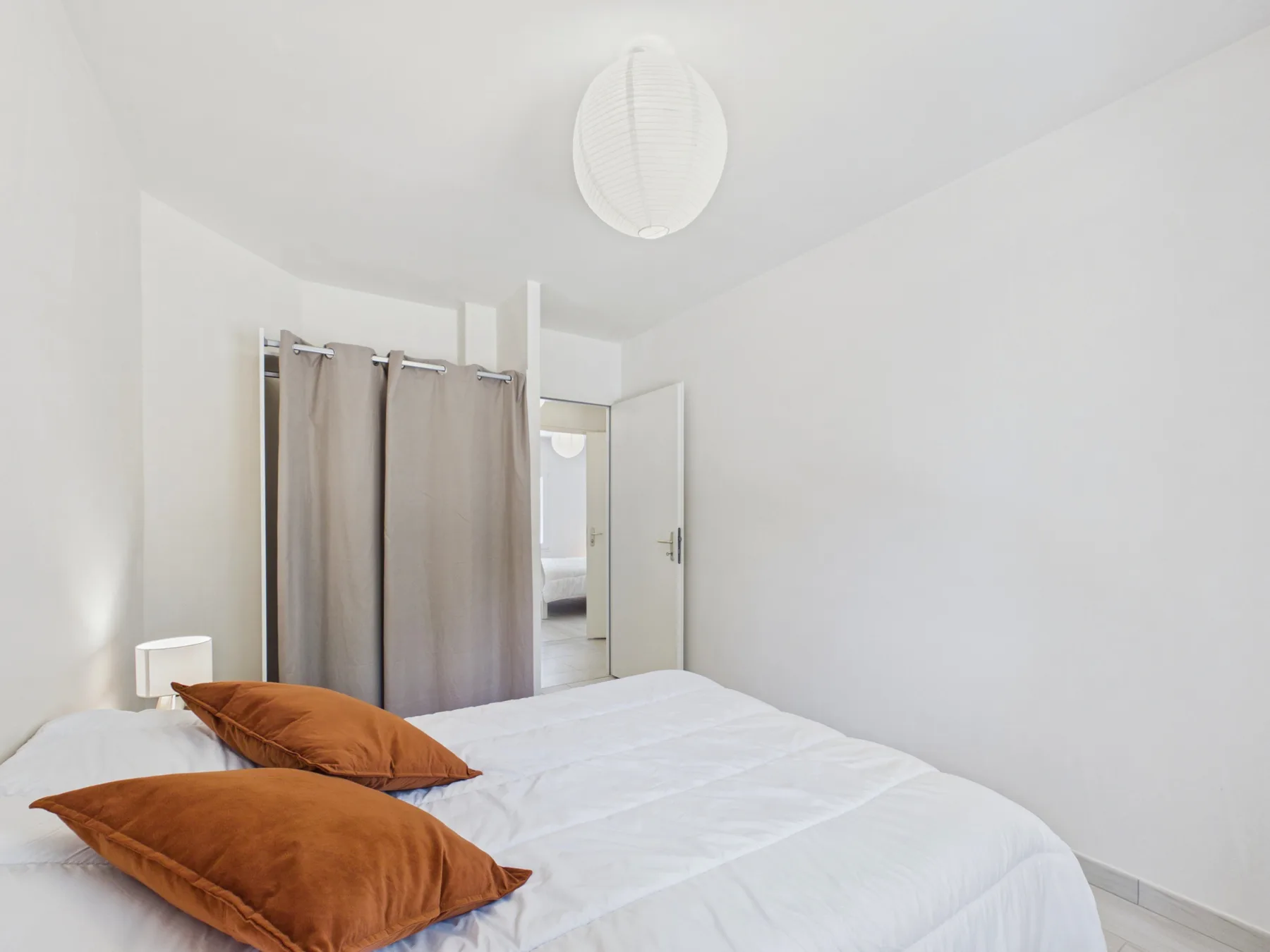 A bright bedroom with white bedding and rust-colored pillows.