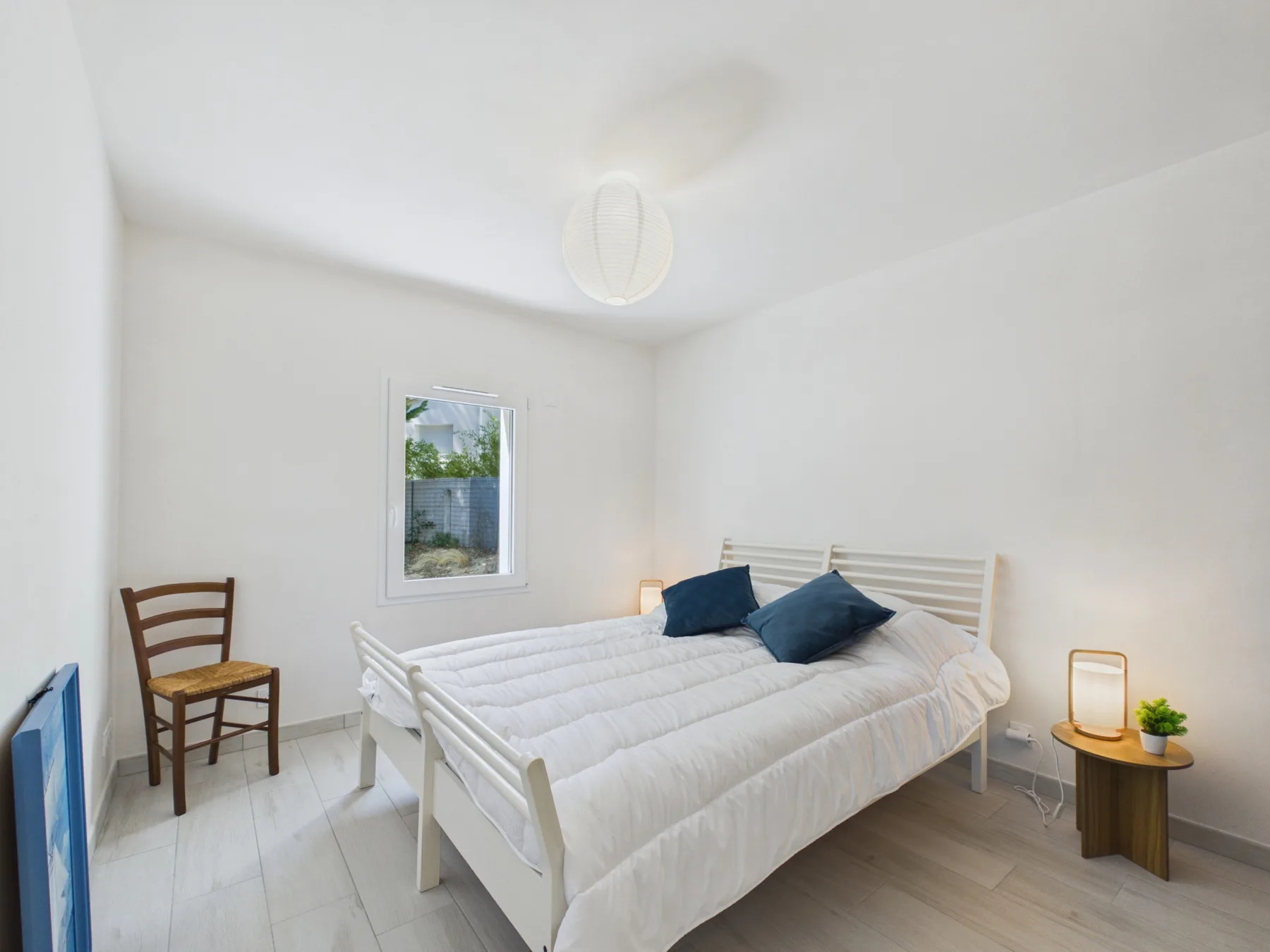 A bright bedroom with a bed, a chair, and a window.