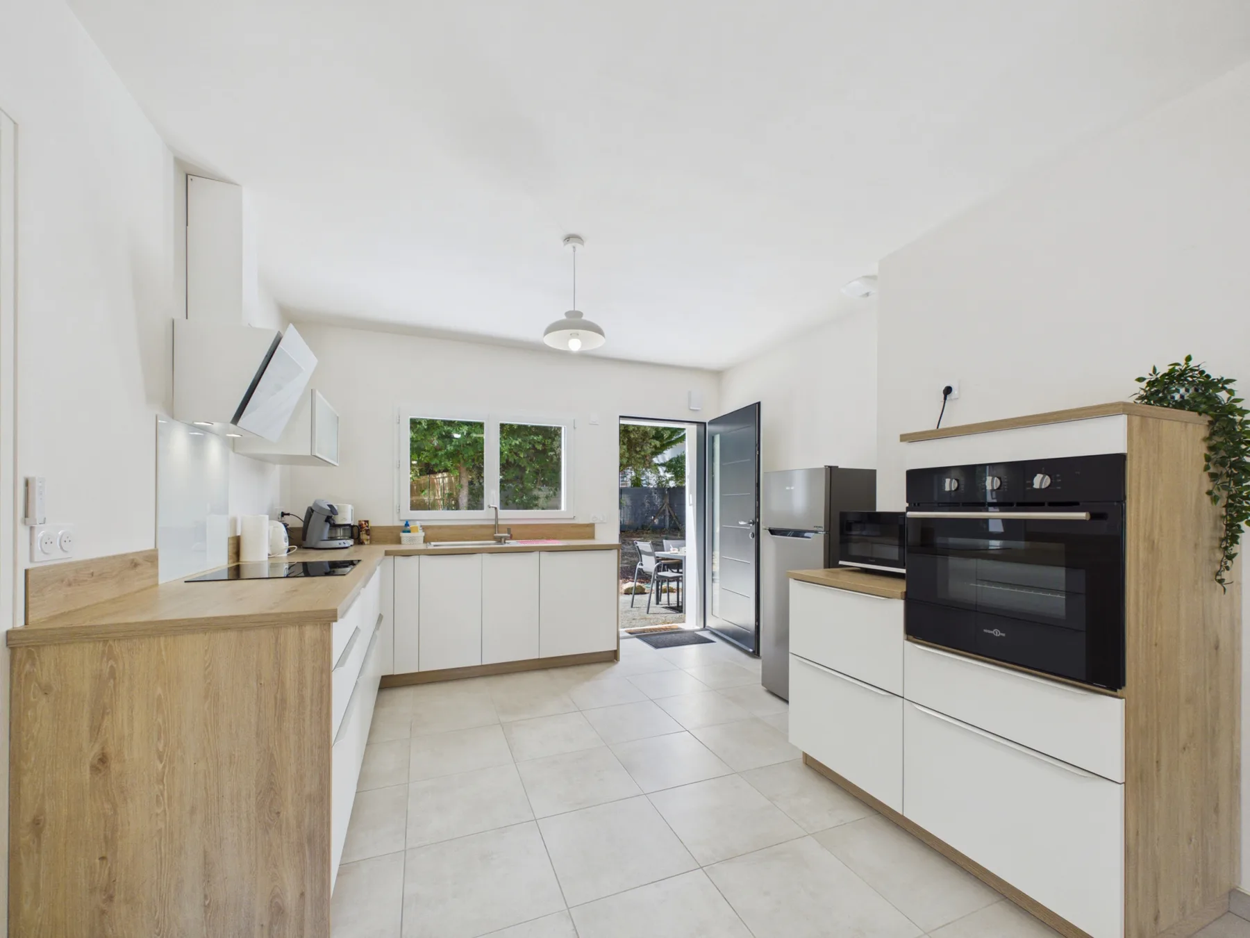 A bright kitchen with white cabinetry, a built-in oven, and windows opening onto a patio.