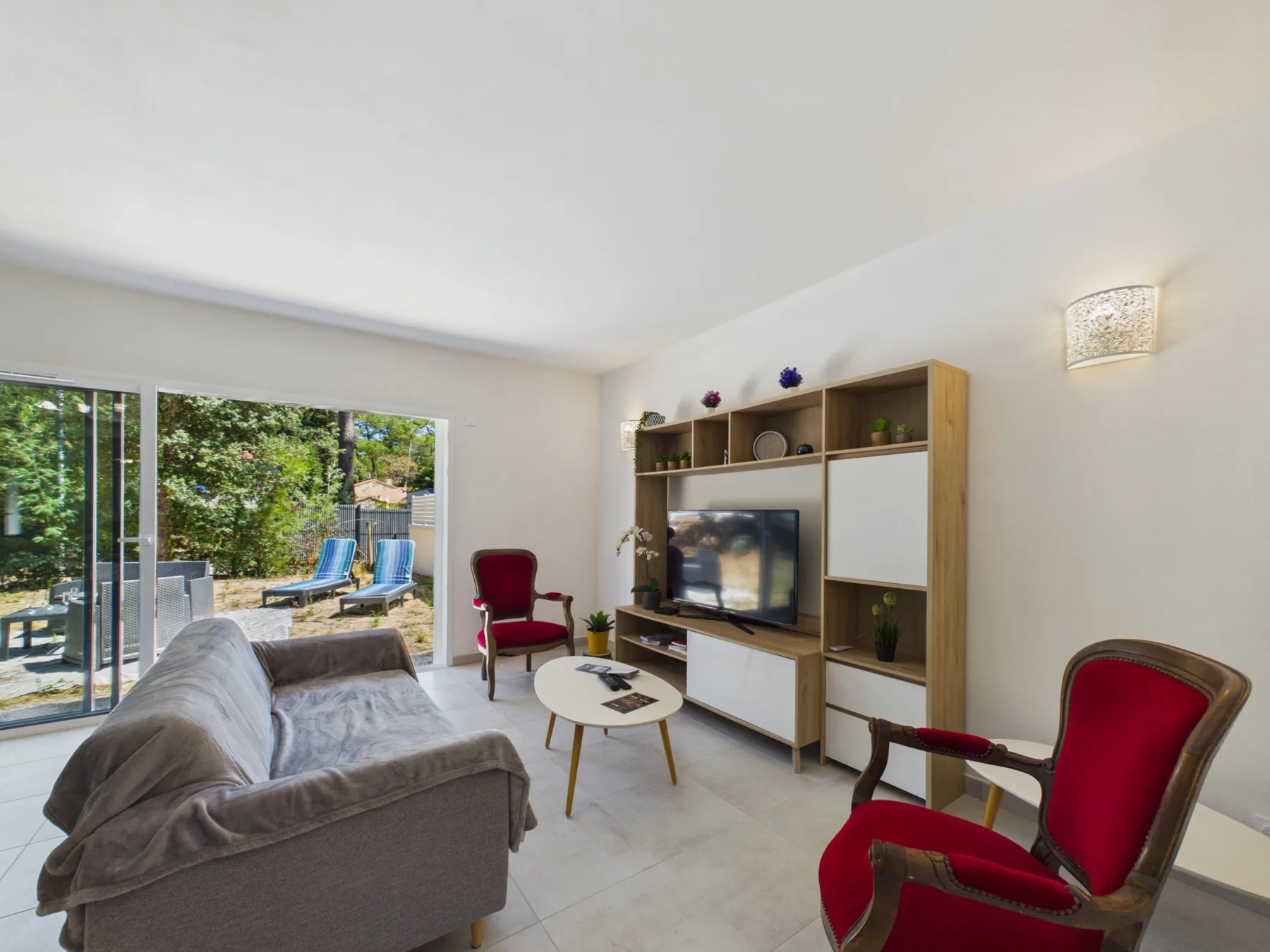 A living room with seating, a television, and sliding glass doors opening to a garden.