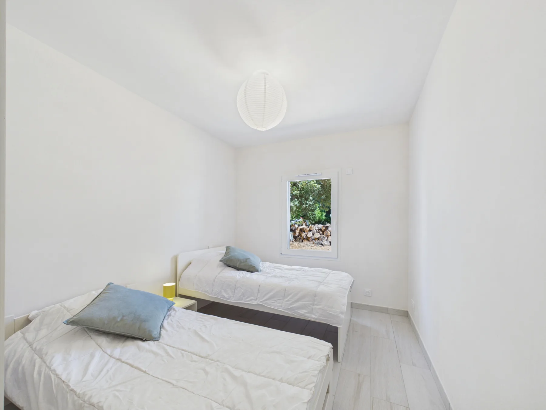 A bright bedroom with two single beds and a small window.