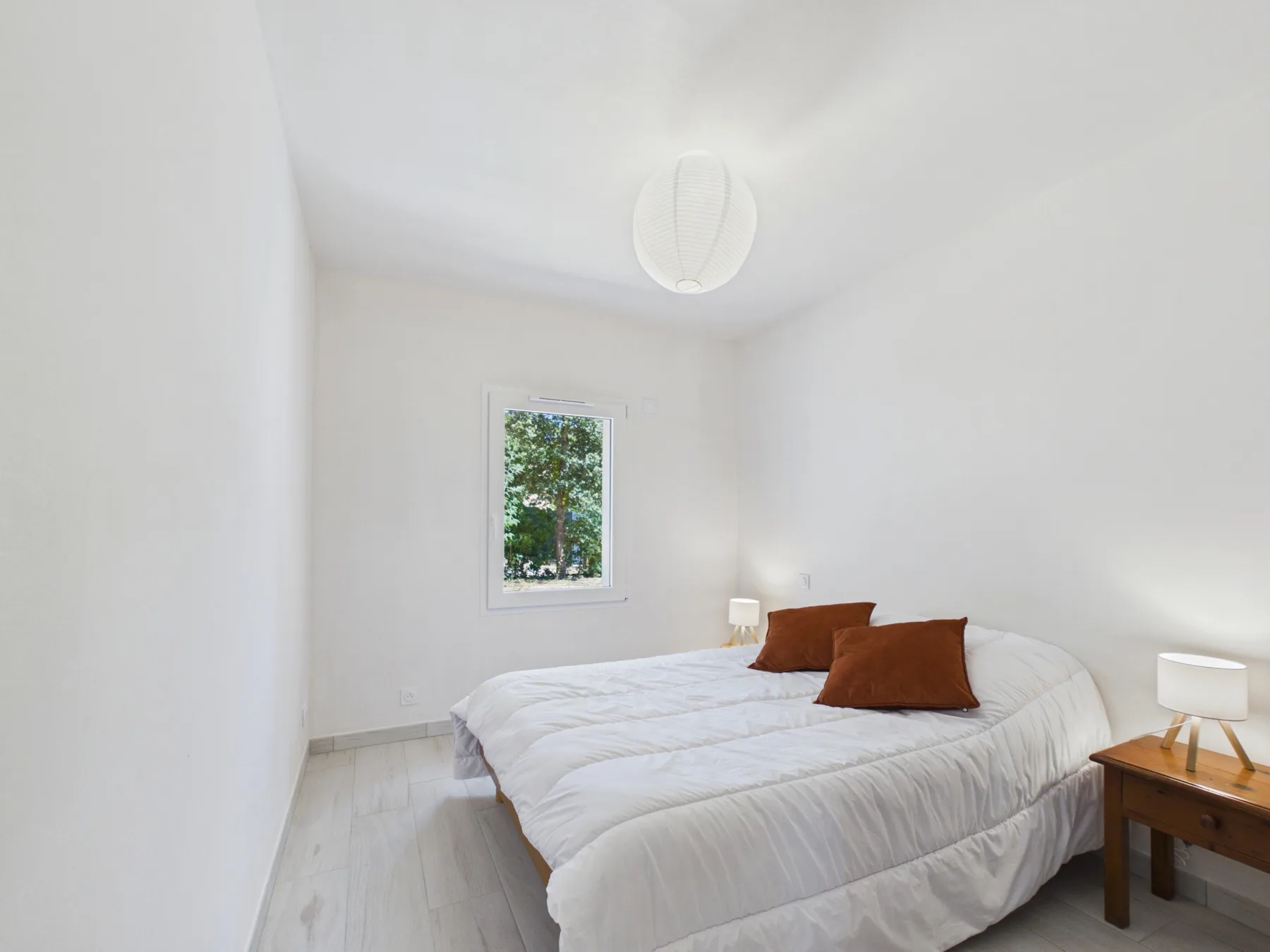 A bright bedroom with a bed and a window overlooking greenery.