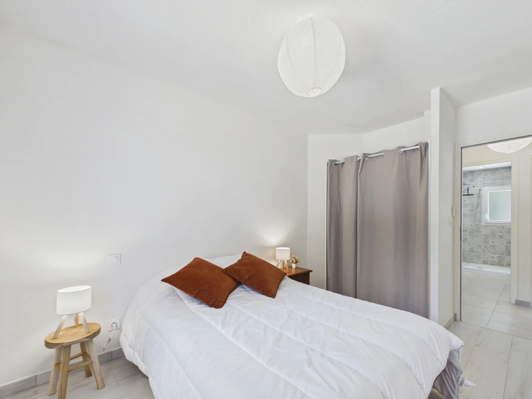 A bright bedroom with a bed and curtains beside an open doorway.