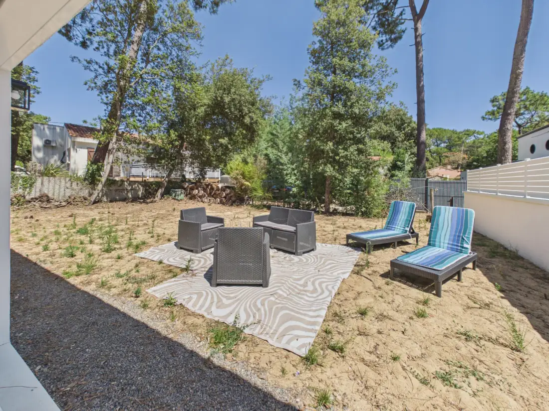 Outdoor seating area with lounge chairs and a striped rug beneath the trees.
