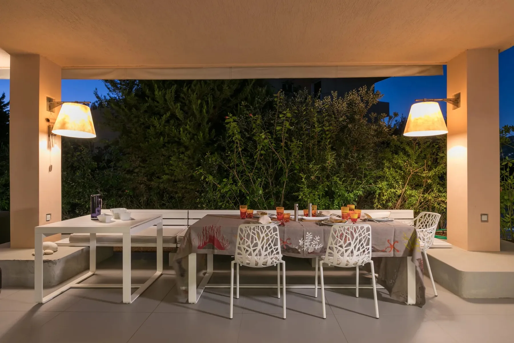 Una zona de comedor al aire libre con una mesa larga y sillas bajo un patio cubierto.