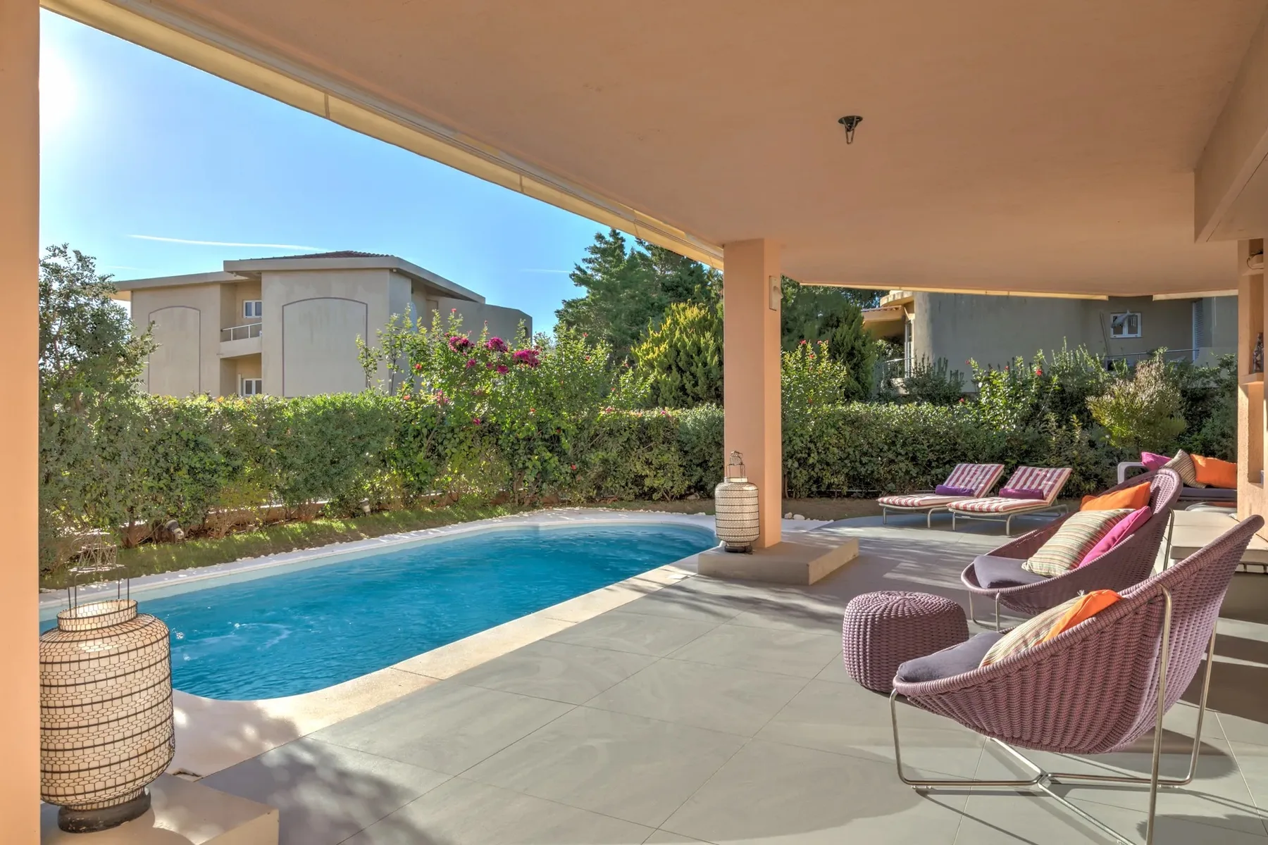 Un patio cubierto con asientos da a una piscina y un jardín.