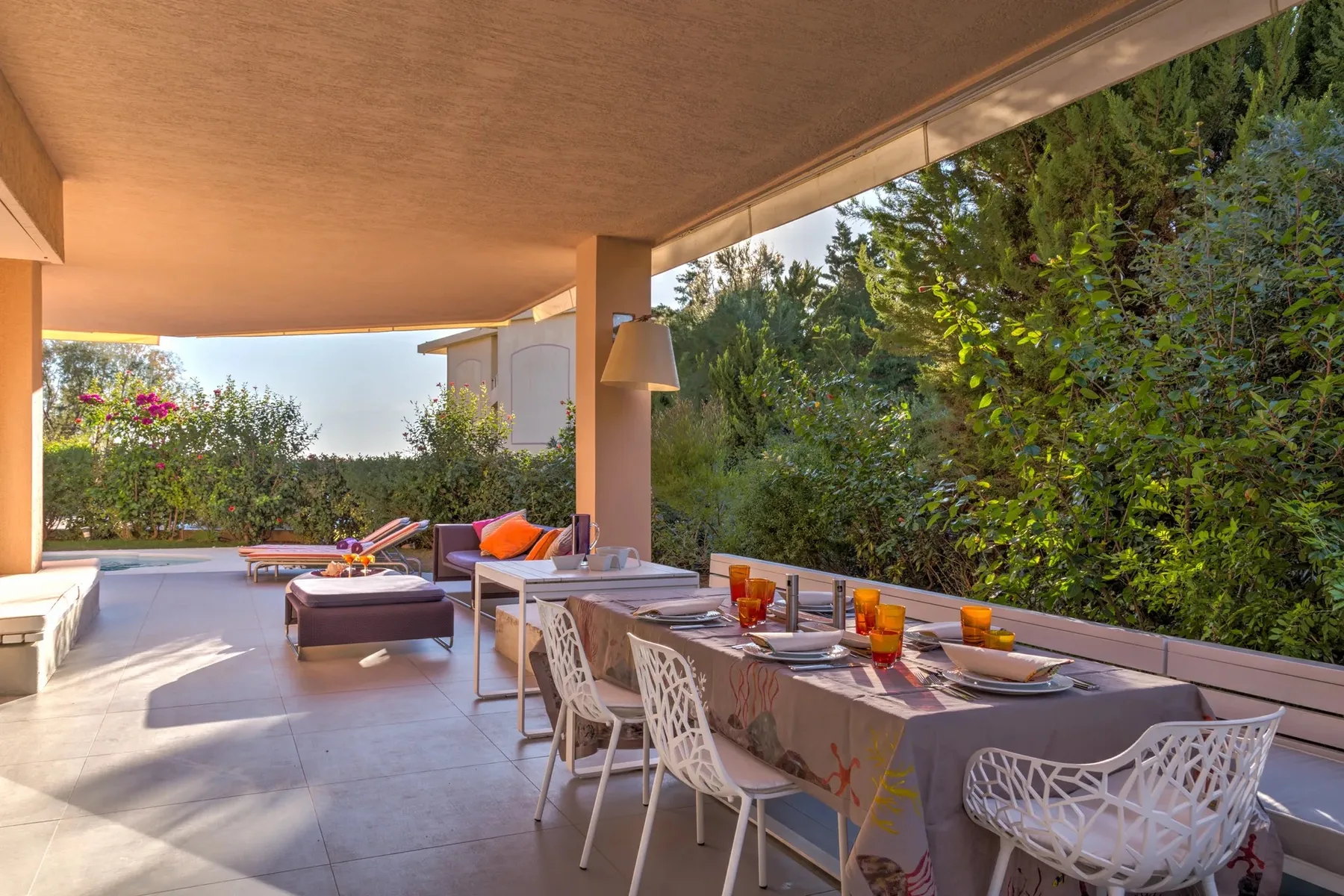 Comedor exterior cubierto con una mesa larga y asientos junto al jardín.