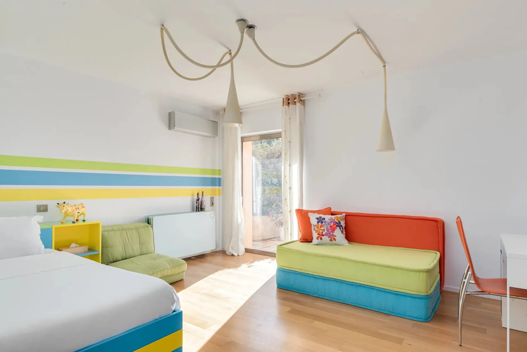 Una sala luminosa con asientos coloridos y una puerta de cristal que da a un balcón.