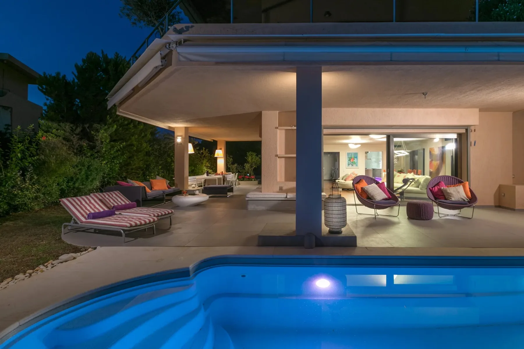 Un patio iluminado con asientos de descanso da a una piscina al anochecer.
