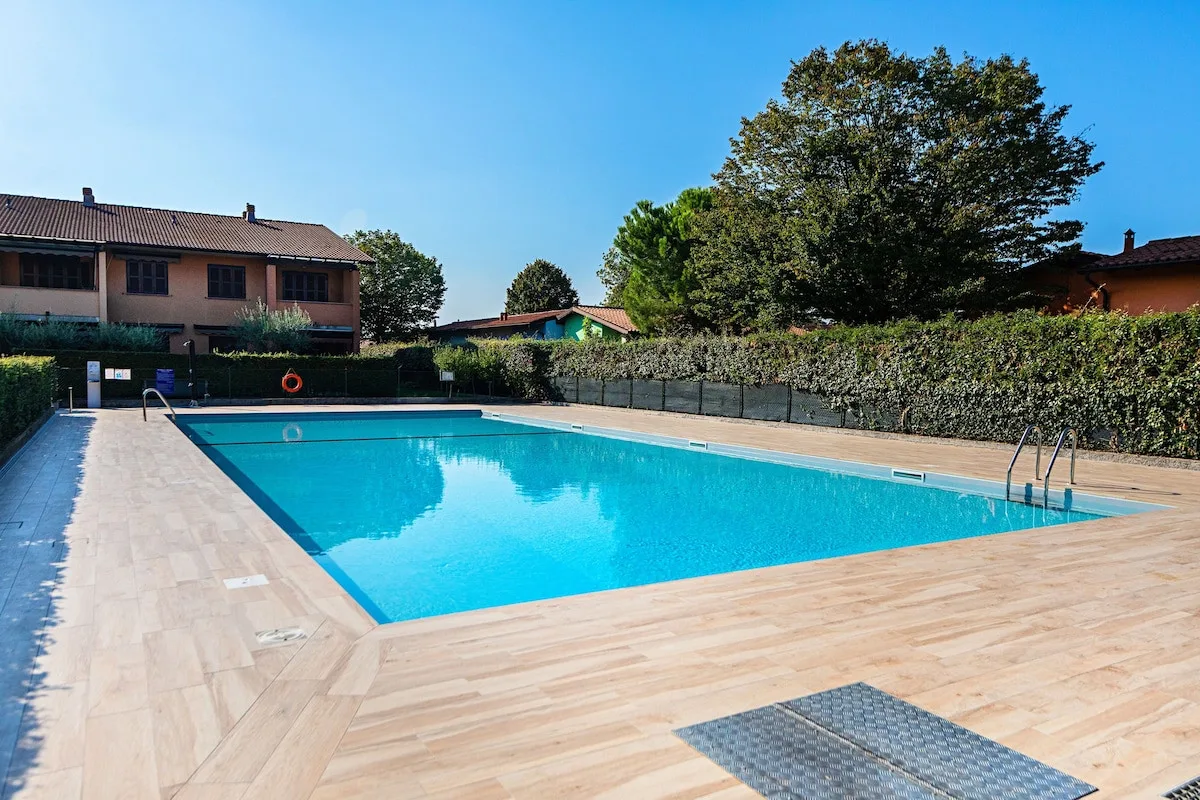 An outdoor swimming pool is surrounded by a pale tiled deck and hedges.