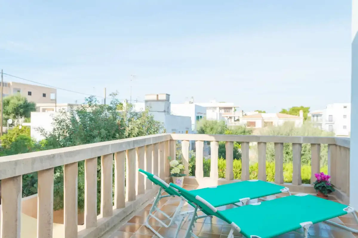 A balcony with turquoise lounge seating overlooks nearby buildings and greenery.