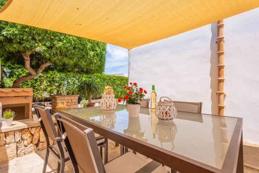 An outdoor dining area sits beneath a yellow shade canopy, with a glass-topped table.