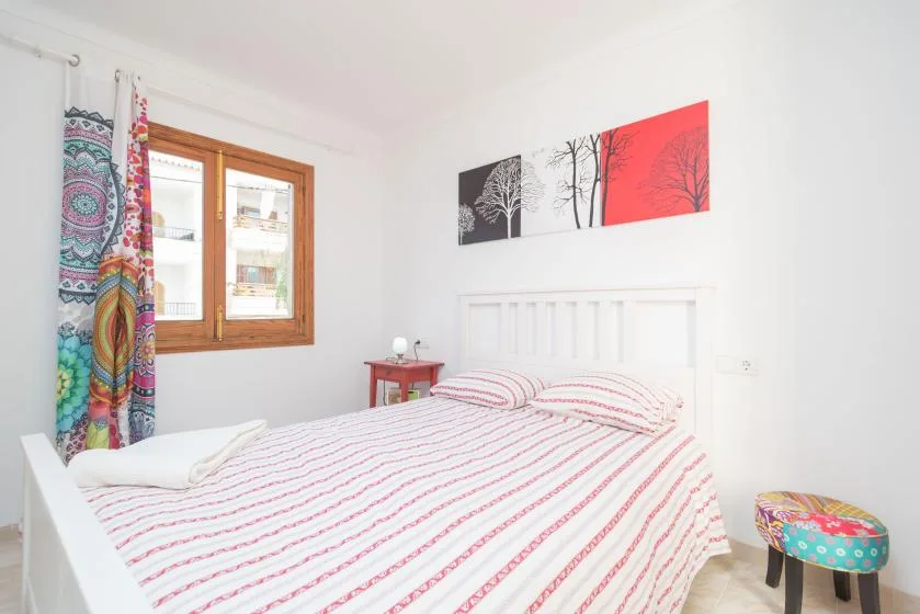 A bright bedroom with a bed beneath colorful tree artwork.