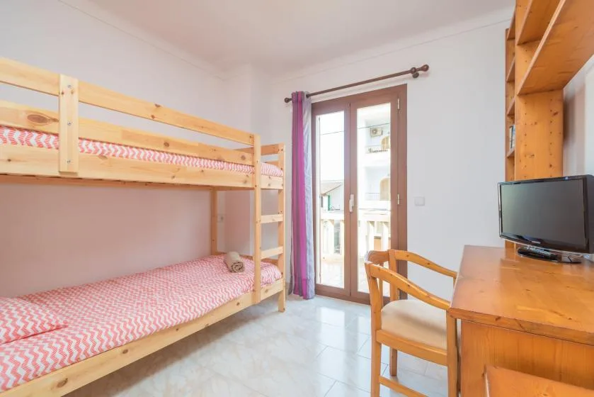 A bedroom with wooden bunk beds and a desk beside glass doors.