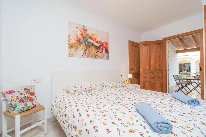 A bedroom with a patterned bedspread, colorful wall art, and wooden doors.