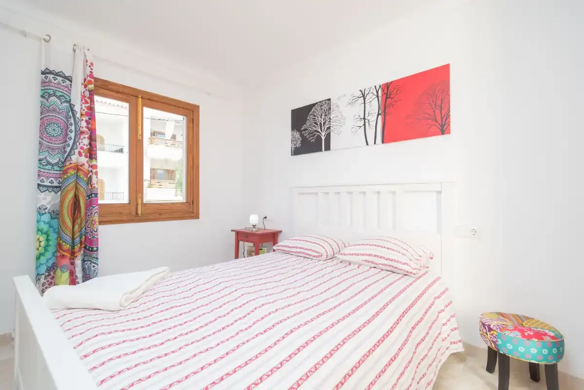 A bedroom with a white bed, striped bedding, and colorful curtains beside the window.