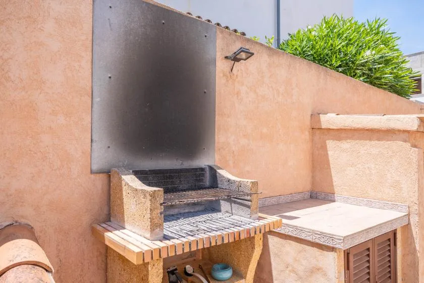 An outdoor barbecue area with a tiled counter and greenery above the wall.
