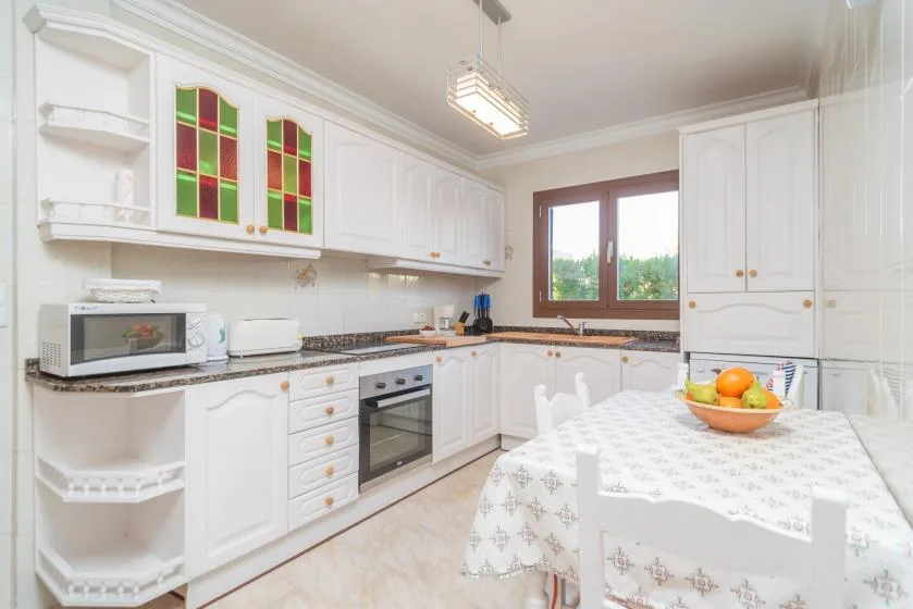 A bright kitchen with white cabinetry and a dining table beside the window.