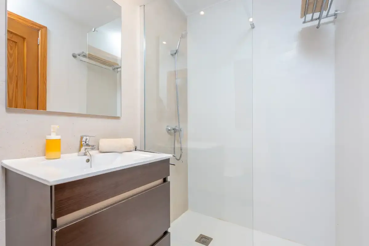 A bright bathroom with a sink, mirror, and shower.