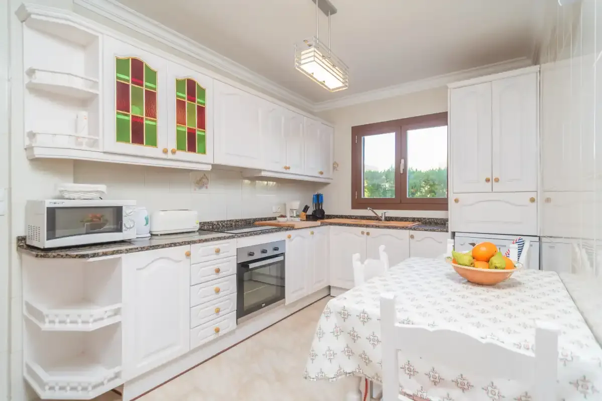 A bright kitchen with white cabinetry, a dining table, and a window.