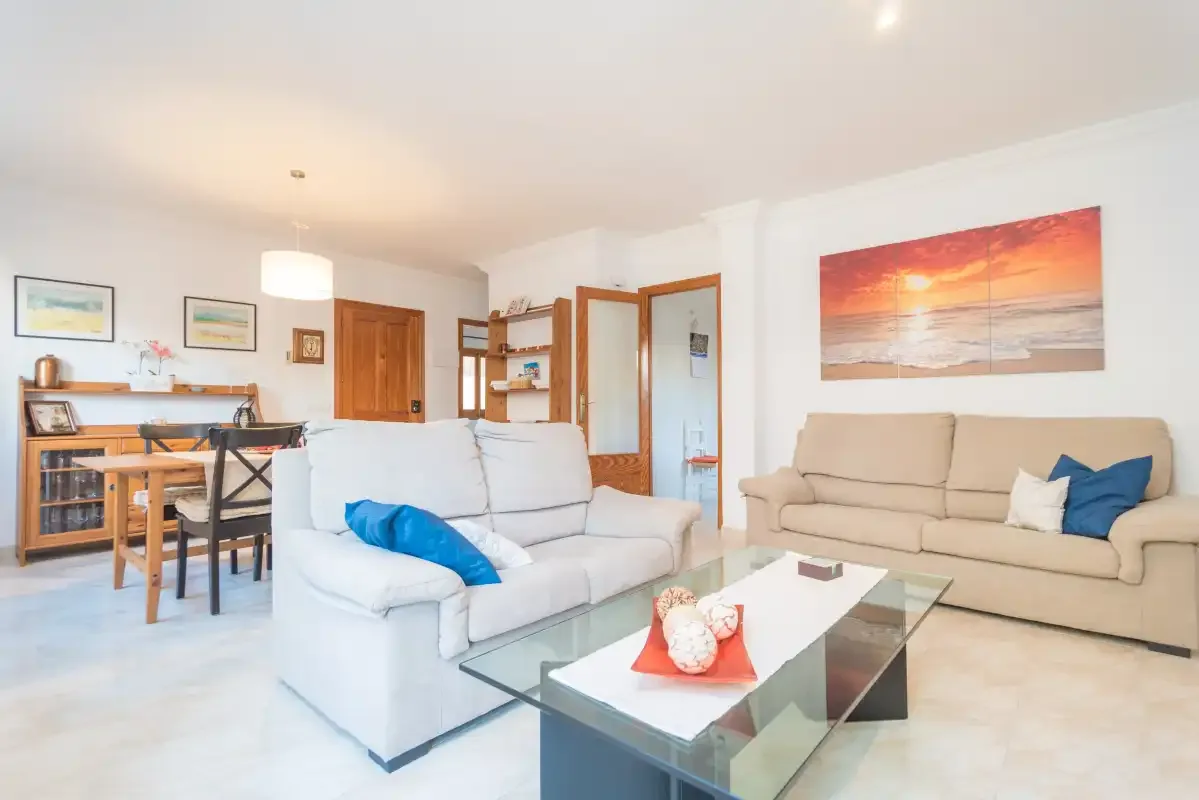A bright living room with seating, a glass coffee table, and a dining area.