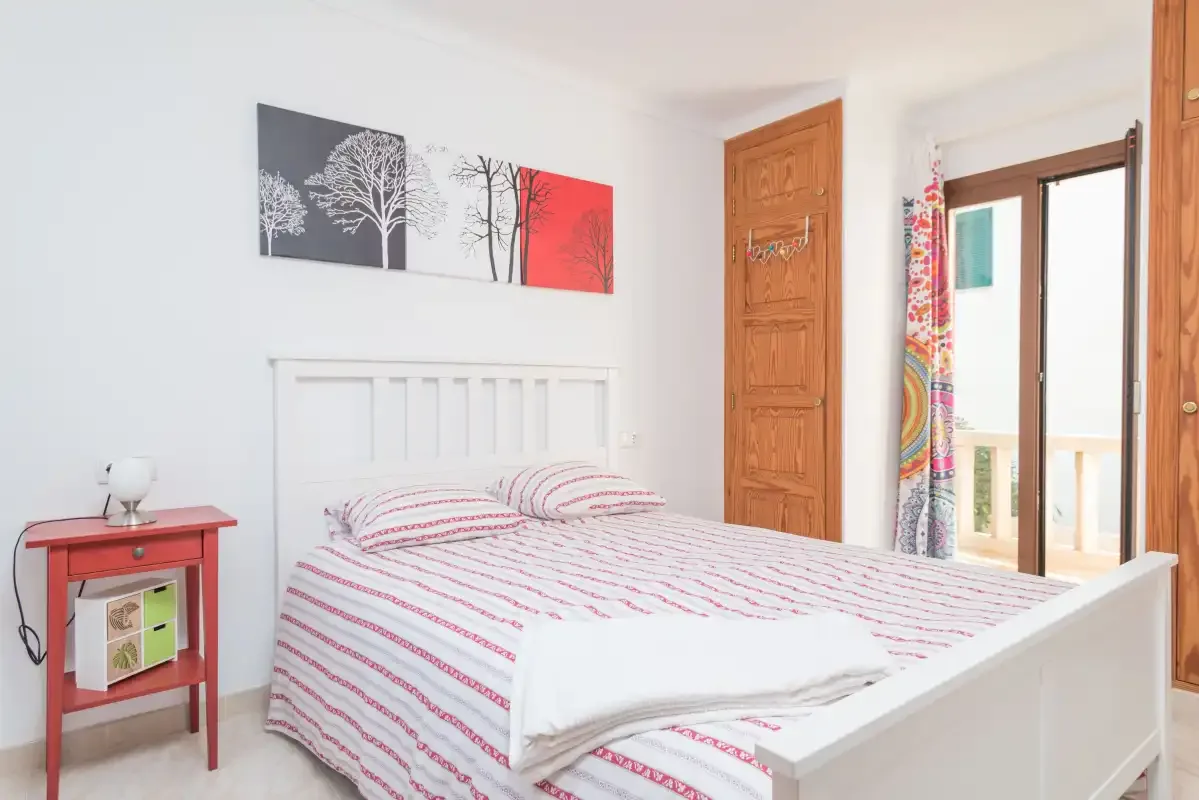 A bedroom with a bed, bedside table, and open balcony doors.